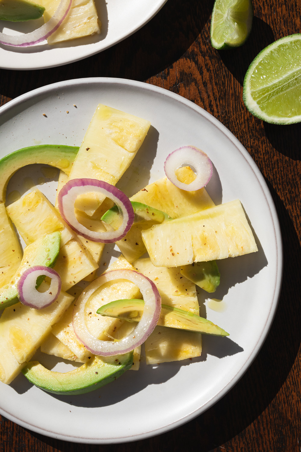 pineapple, avocado, and red onion salad on white plates on a wooden table with lime slices